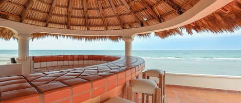 Un bar en la playa con techo de paja, asientos al aire libre y vista al océano.