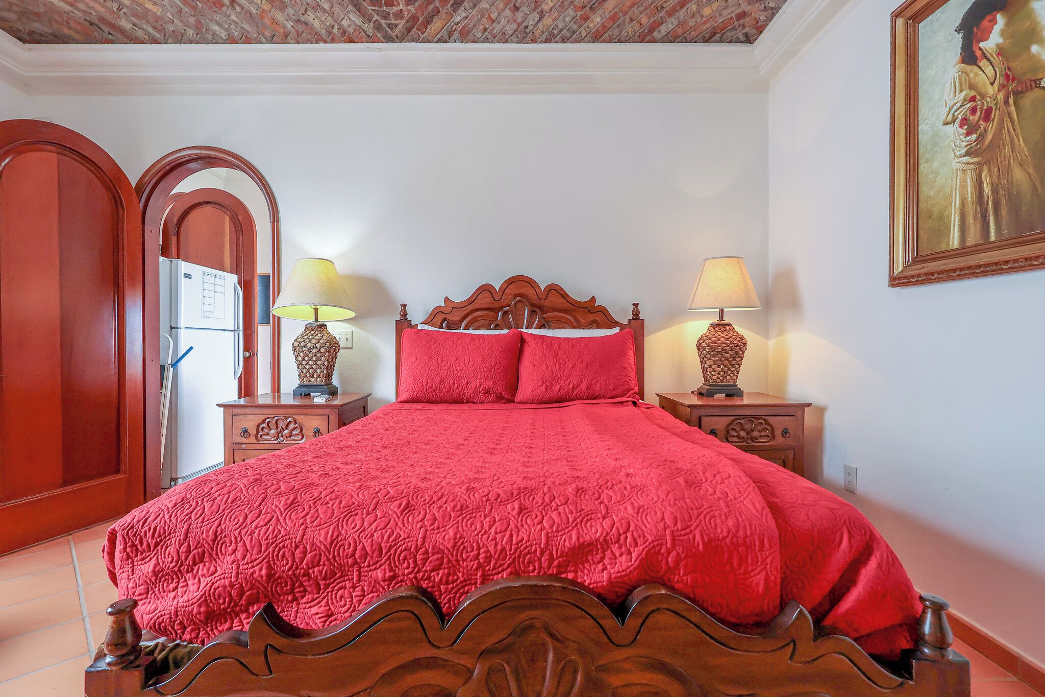 Una camera da letto con un letto in legno, due comodini con lampade, una coperta rossa e un quadro appeso al muro.