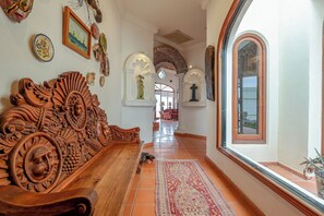 Ein Flur mit einer Holzbänkl, dekorativen Wandverzierungen, einem roten Teppich mit Muster und einem großen Bogenfenster.