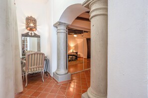 Ein Flur mit Spiegel, Stuhl, Lampe und einem Bett im Hintergrund.