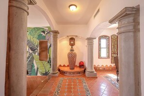 Un couloir orné de colonnes, doté d’un sol carrelé, d’un vase décoratif et d’une fresque murale.