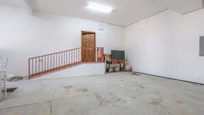 Ein Zimmer mit Betonboden, einer Holztür, einer roten Metalltreppe und einem kleinen Tisch mit Stuhl.