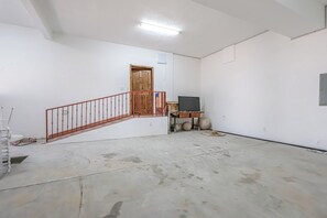 Ein Zimmer mit Betonboden, einer Holztür, einer roten Metalltreppe und einem kleinen Tisch mit Stuhl.
