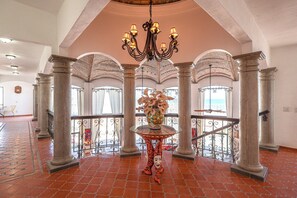 A grand lobby with a chandelier, columns, a glass table with a vase, and a view through the balcony railing. - Casa Elegante – Ocean View Estate, Rocky Point (Puerto Peñasco)