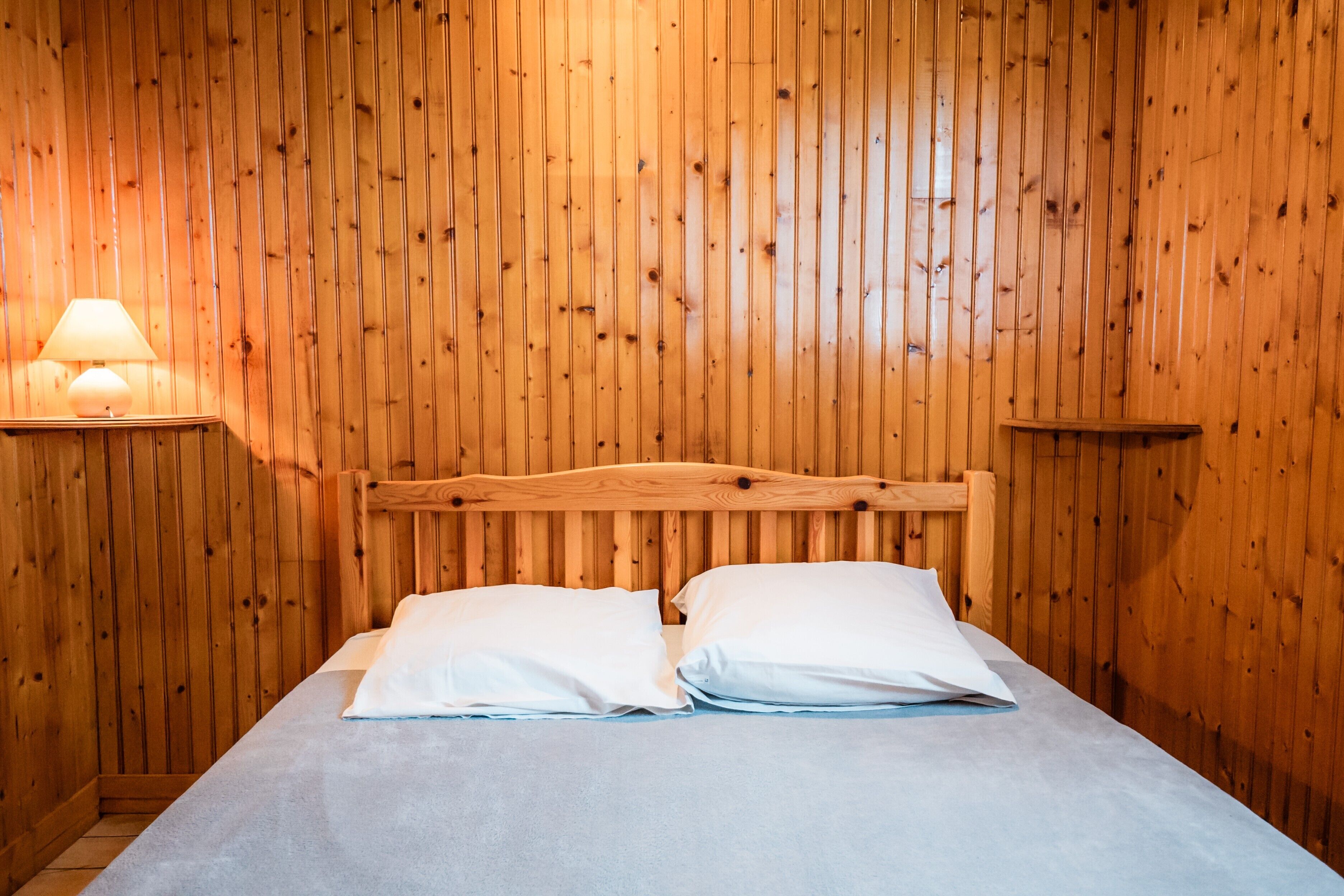 Een kamer met houten lambrisering, een bed, kussens en een nachtkastje met een lamp.