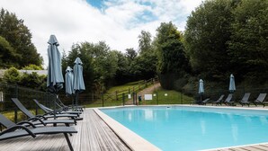 A swimming pool with lounge chairs and umbrellas, surrounded by trees. - Chalet Noël des Champs for 8 with Shared Pool, Terrace, and Wi-Fi (Livarot-Pays-d'Auge)