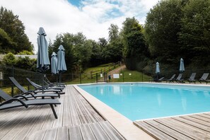 A swimming pool with lounge chairs and umbrellas, surrounded by trees. - Chalet Noël des Champs for 8 with Shared Pool, Terrace, and Wi-Fi (Livarot-Pays-d'Auge)