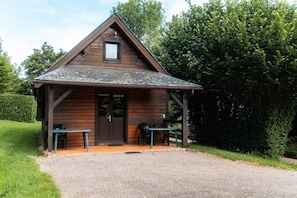 A small wooden cabin with a pitched roof, a door, and a window. - Chalet Noël des Champs for 8 with Shared Pool, Terrace, and Wi-Fi (Livarot-Pays-d'Auge)