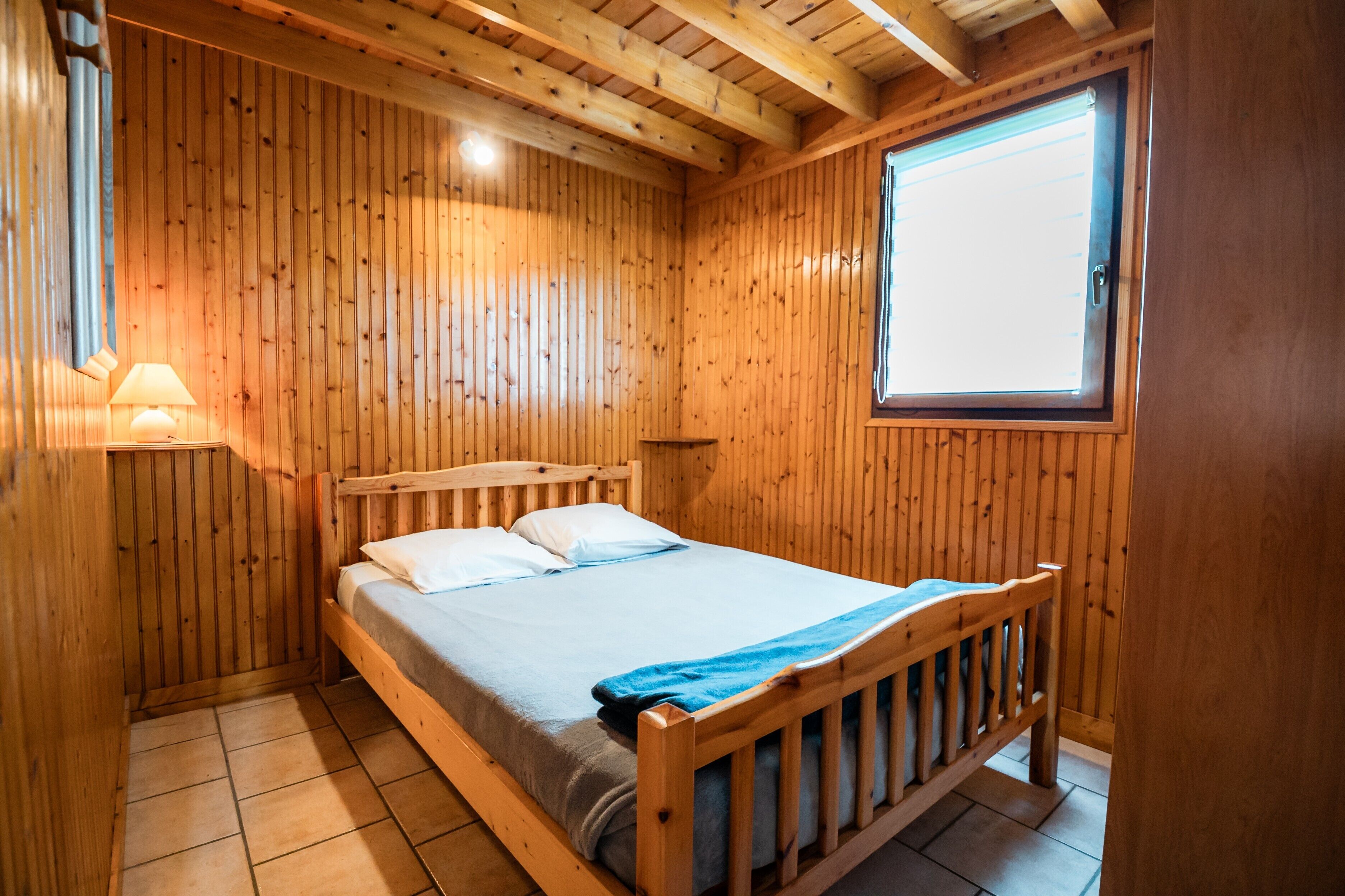 Une pièce aux murs lambrissés, avec un lit simple, une fenêtre et une lampe.