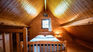 A wooden cabin bedroom with a bed, a window with curtains, and a small wall-mounted picture. - Chalet Noël des Champs for 8 with Shared Pool, Terrace, and Wi-Fi (Livarot-Pays-d'Auge)