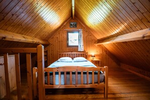 A wooden cabin bedroom with a bed, a window with curtains, and a small wall-mounted picture. - Chalet Noël des Champs for 8 with Shared Pool, Terrace, and Wi-Fi (Livarot-Pays-d'Auge)