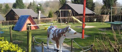 A fenced area with a sculpture of a cow, a playground with swings and slides, and a building with a sloped roof.