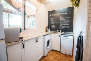 Una cocina con un menú en pizarra, lavadora, lavavajillas y ventana con vistas al verdor.