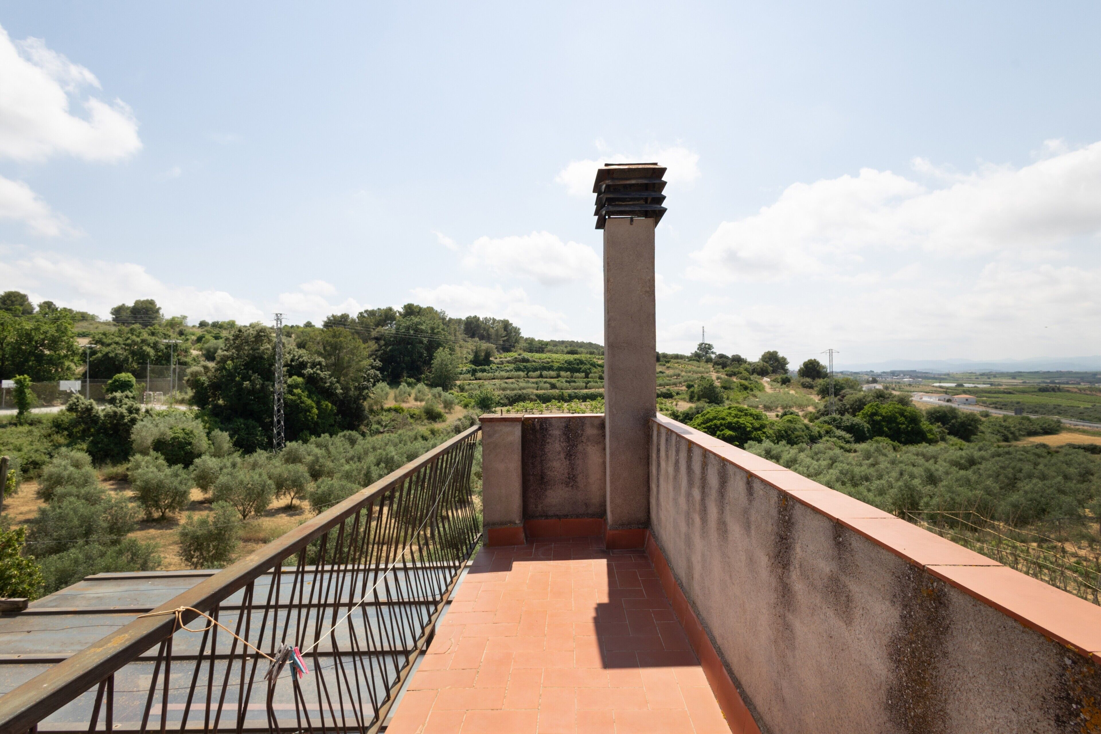Un balcone con vista su un paesaggio collinare, una colonna in cemento e una ringhiera metallica.