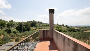 Un balcone con vista su un paesaggio collinare, una colonna in cemento e una ringhiera metallica.
