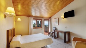 Une chambre avec un lit, un bureau, une chaise, une télévision et un balcon avec vue.