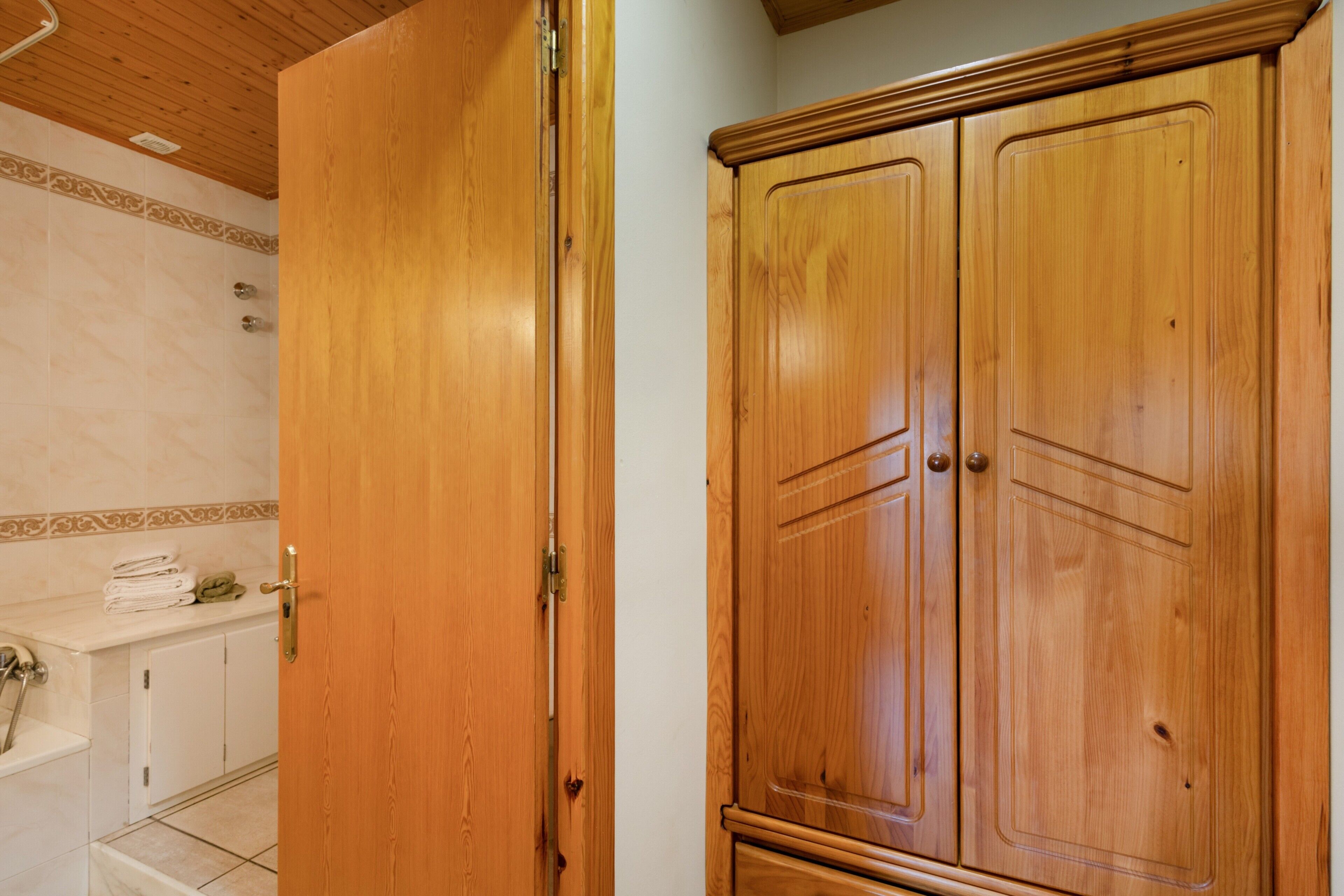 A wooden wardrobe with two doors, a bathroom with a sink and a toilet, and a shower area.
