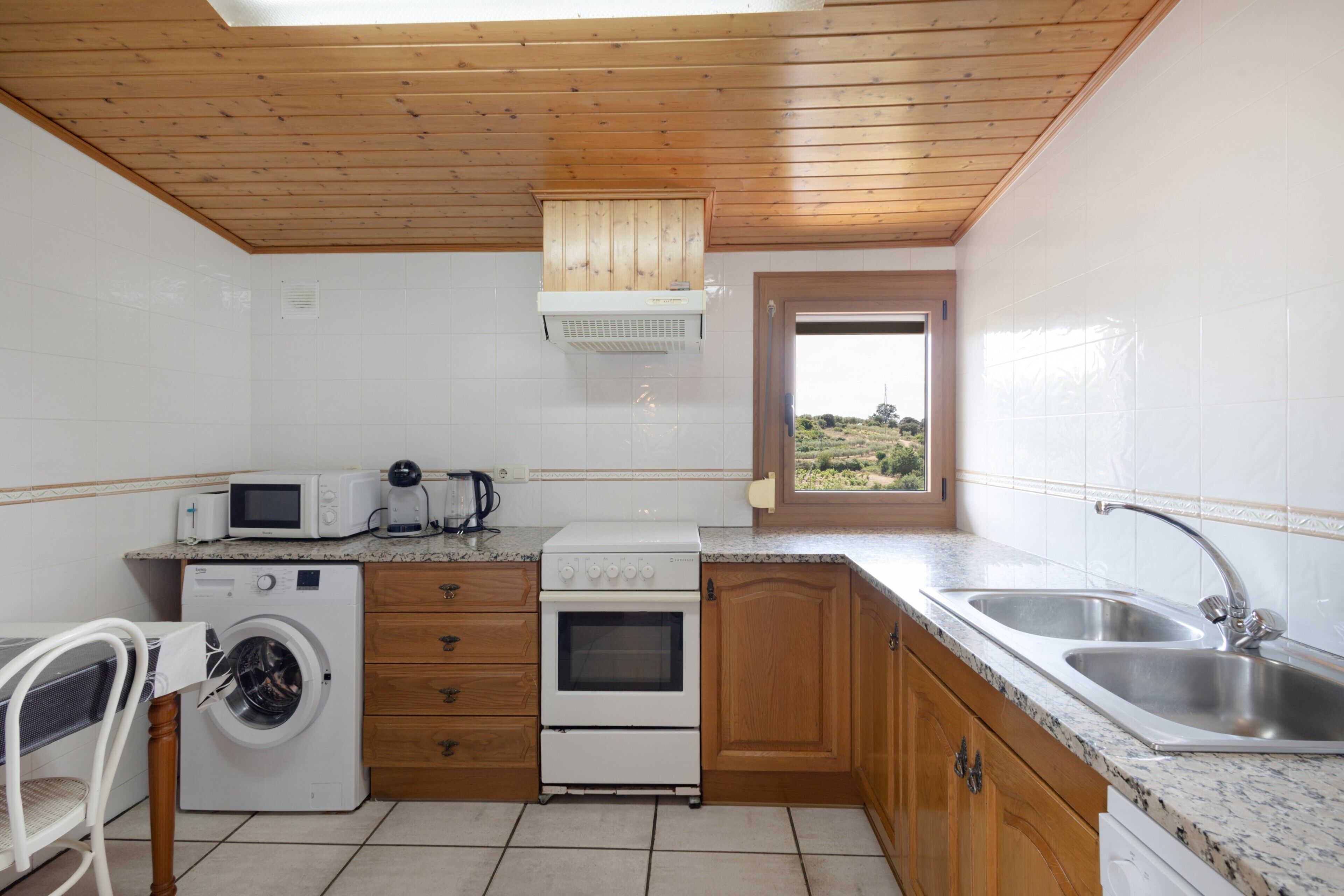 Een compacte keuken met een wasmachine, magnetron, oven en een raam met uitzicht.