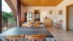 Un espace repas comprenant une grande table, des chaises, un buffet et donnant sur l’extérieur.