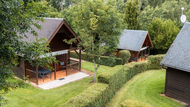 Deux cabanes en bois, chacune dotée d’une véranda attenante, sont entourées de pelouses bien entretenues et d’une végétation dense.