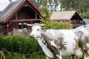 A cow statue in front of a rustic wooden building with a sloped roof.