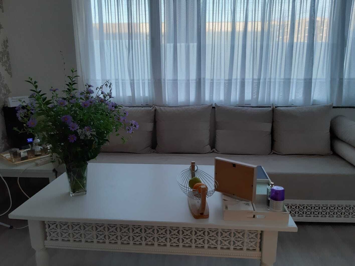 Een woonkamer met een bank, een salontafel en een raam met dunne gordijnen.