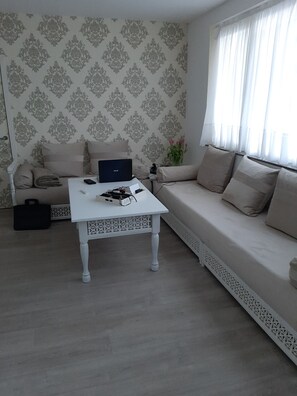 En stue med sofa, sofabord, en bærbar computer, en vase med blomster og tapet med mønster.