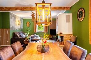 Un coin repas avec une table en bois, des chaises, un luminaire suspendu et un mur vert ornĂ© dâune horloge.