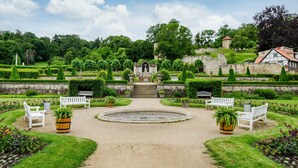 Een formele tuin met een centraal standbeeld, witte banken en een fontein.