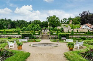 Un jardin à la française avec une statue centrale, des bancs blancs et une fontaine circulaire.