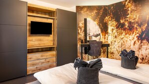 Een moderne hotelkamer met een flatscreen televisie, een houten kledingkast, een bed met handdoeken en een muurschildering.