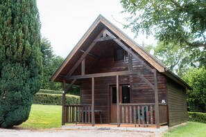 A wooden cabin with a porch, a door, and a small window. - Chalet Calard 6p with Shared Pool, Private Terrace and Wi-Fi (Livarot-Pays-d'Auge)