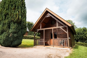 Eine Holzhütte mit Veranda, einem großen Baum und einem gepflegten Rasen.