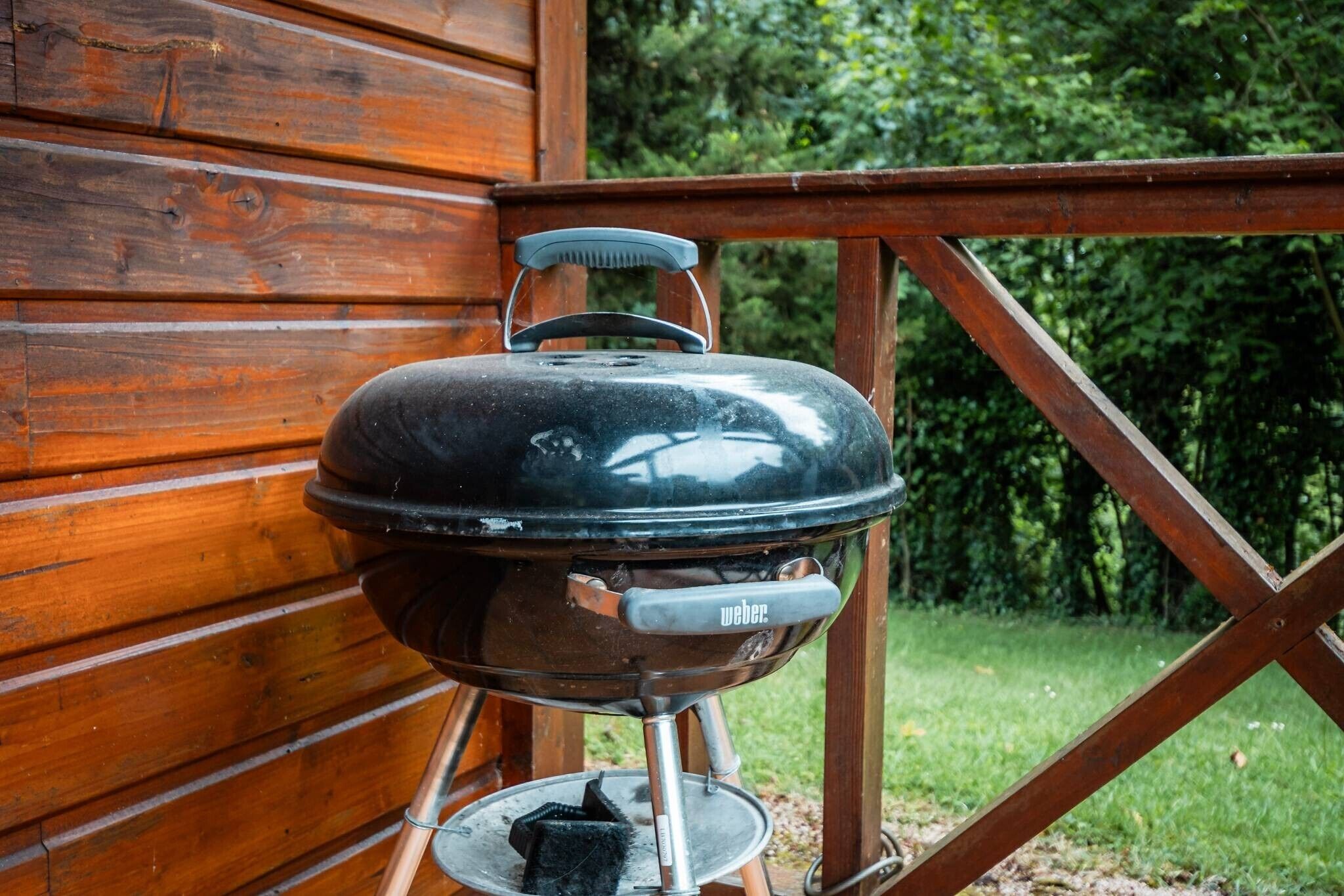 Una griglia Weber con coperchio, posizionata su un supporto all'esterno di un edificio in legno.