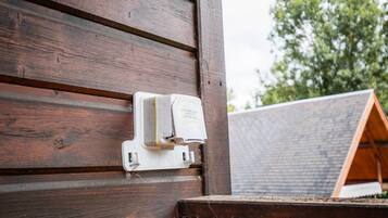 Een houten buitenmuur met een witte elektrische kast.