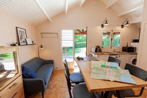 A compact kitchen with a dining area, a sofa, and a map on the table. - Domaine de Guillaume, Chalet Frequin 4p with Shared Pool, Wi-Fi (Livarot-Pays-d'Auge)