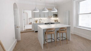 A modern kitchen with a central island, pendant lights, and a view of the adjacent dining area. - The Bridge York - Stunning River Front Location (York)
