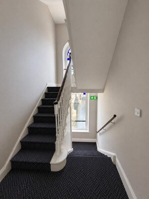 A staircase with a herringbone carpet pattern, white walls, and a view of a body of water through a window. - The Bridge York - Stunning River Front Location (York)