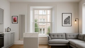 A modern kitchen with a white countertop, a grey sofa, and a radiator. - The Bridge York - Stunning River Front Location (York)