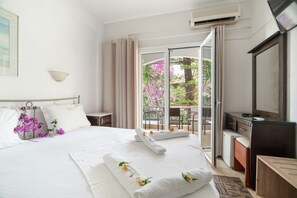 A hotel room with a bed, a desk, a TV, and a balcony with a view of trees and flowers. - Room 'Double  117' with Shared Terrace, Wi-Fi and Air Conditioning (Nikiana)