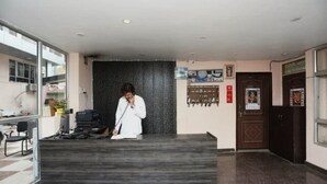 En receptionsdisk med en person bag den, en mørk væg med struktur, en dør med detaljeret panel og et vindue til venstre.