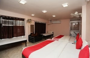 A hotel room with two beds, a bench, a desk, a chair, a fan, and an air conditioning unit. - SHREE KRISHNA HOTEL INN (Varanasi)
