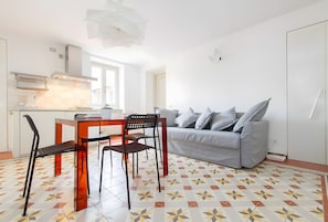 A compact living space with a kitchenette, a dining area with a table and chairs, and a grey sofa.
