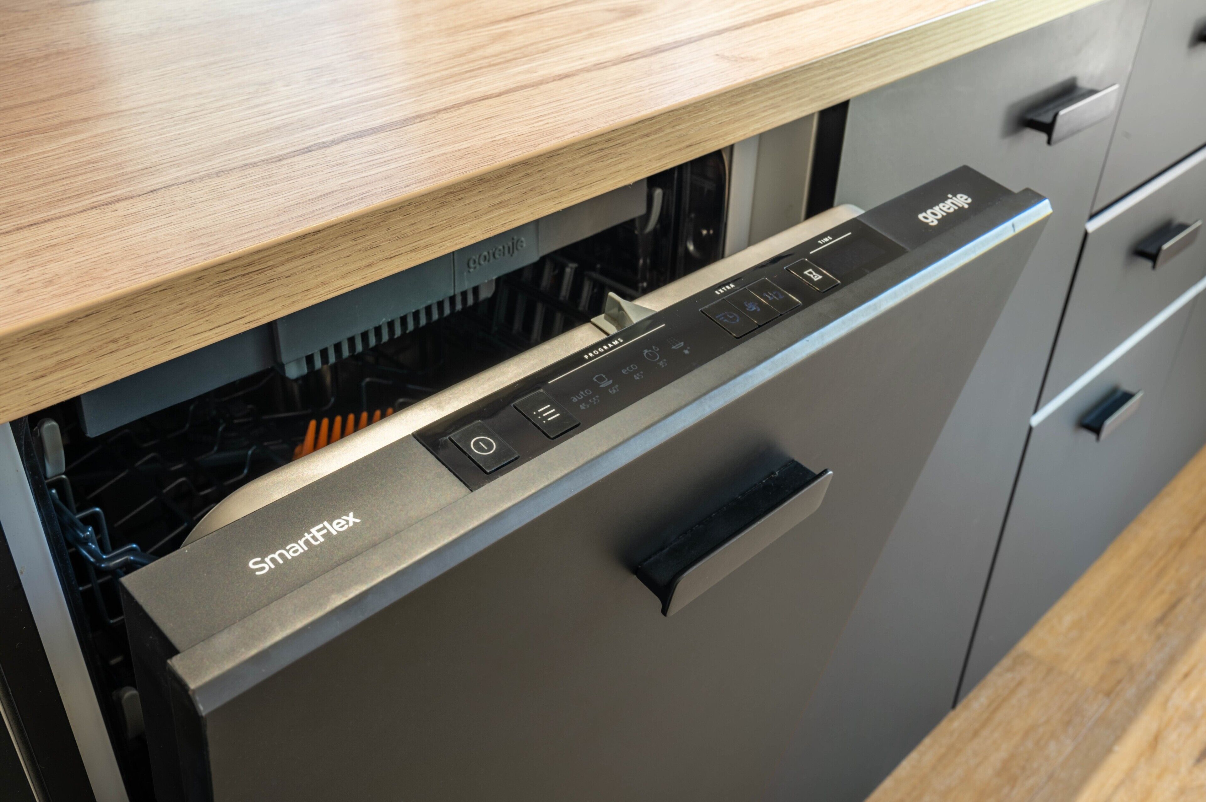 A modern kitchen with a built-in dishwasher, a wooden countertop, and a grey cabinet with a handle.