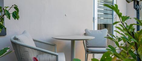A patio with wicker chairs and a round table, a glass door leading inside, and potted plants.