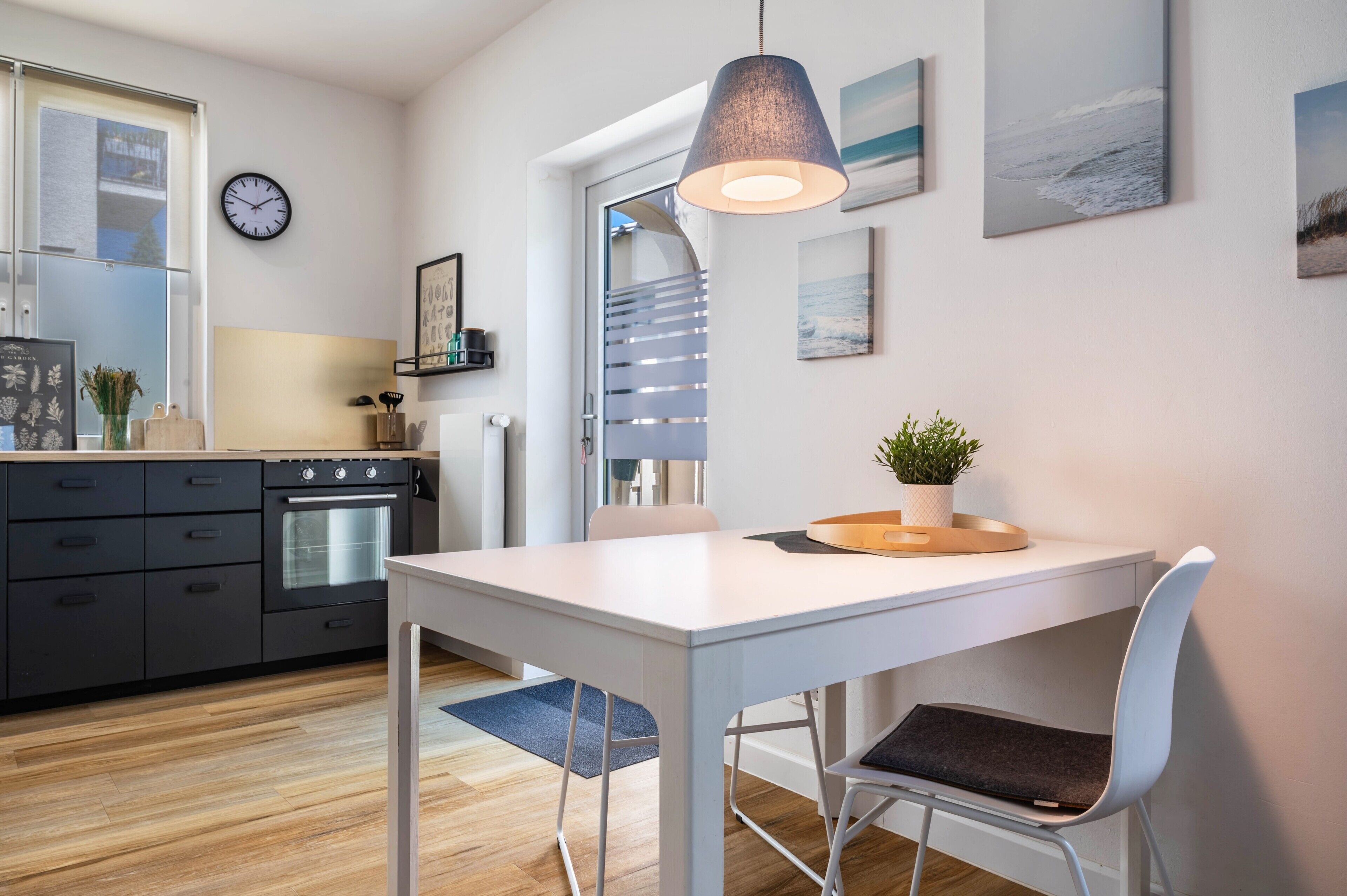 Een moderne keuken met een witte tafel, een klok en een hanglamp.