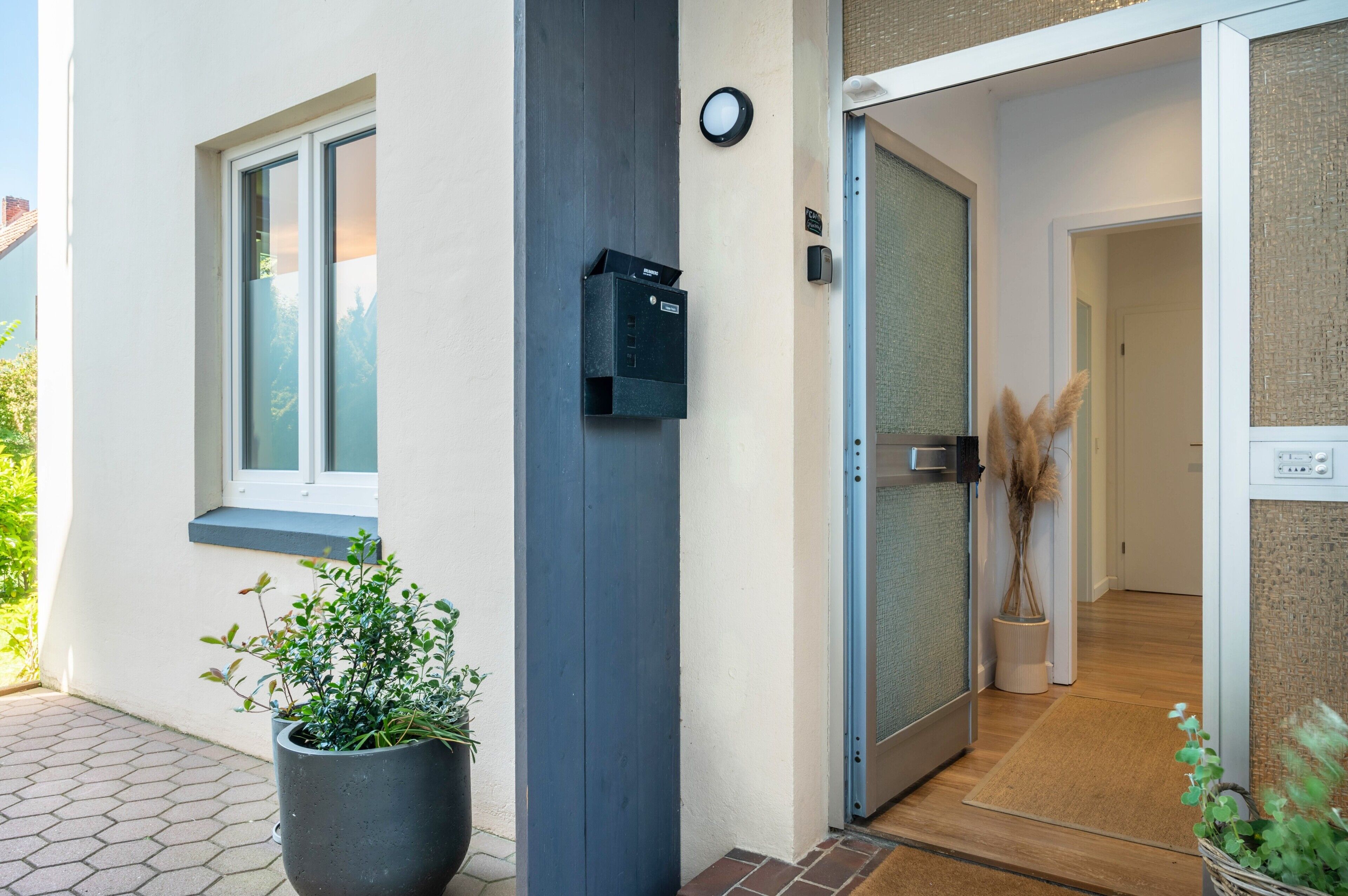 A modern building entrance with a mailbox, a potted plant, and a door leading inside.
