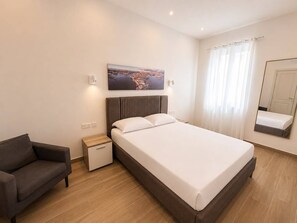 A hotel room with a bed, a nightstand, a sofa, a painting on the wall, a window with curtains, and a mirror. - Maisonette 2 Bedroom in quaint Qala with AC for relaxing stays next to Square (Qala)