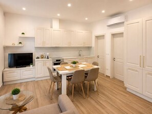 A modern kitchen with white cabinets, a dining table with chairs, a TV, and a small plant on the counter. - Maisonette 2 Bedroom in quaint Qala with AC for relaxing stays next to Square (Qala)