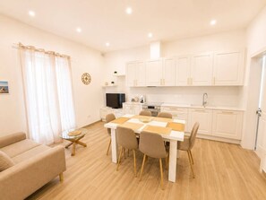 A modern kitchen with white cabinets, a dining table with chairs, a TV, and a small island with a glass top. - Maisonette 2 Bedroom in quaint Qala with AC for relaxing stays next to Square (Qala)